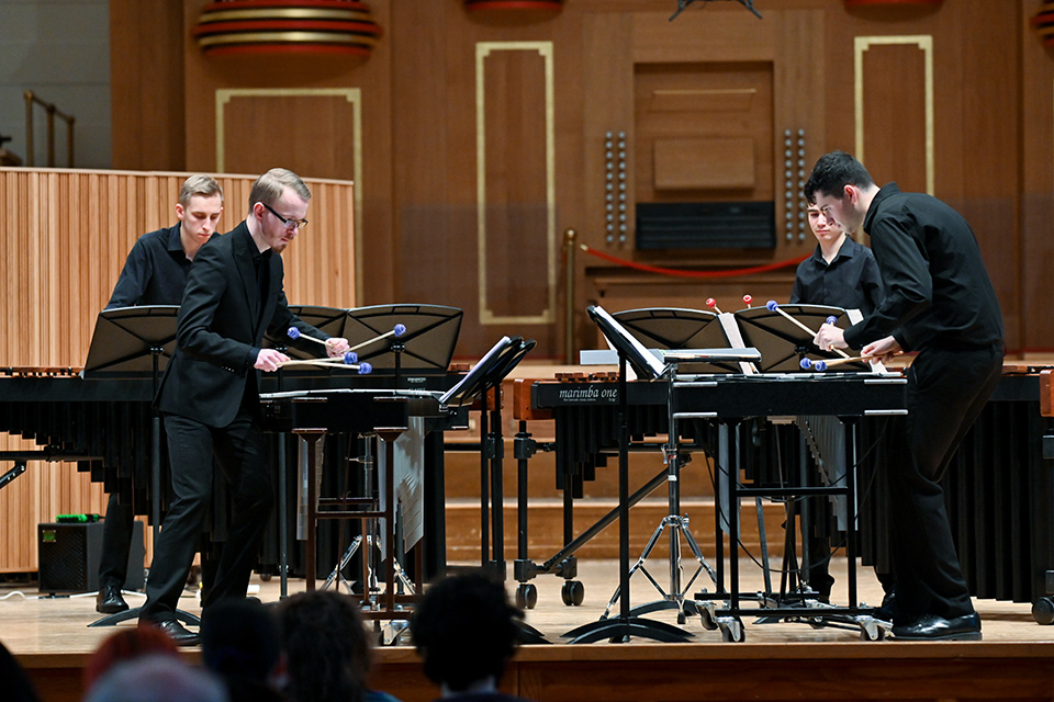 Four students on stage in the RCM's Amaryllis Fleming Concert Hall, playing the marimbas and xylophones to an audience
